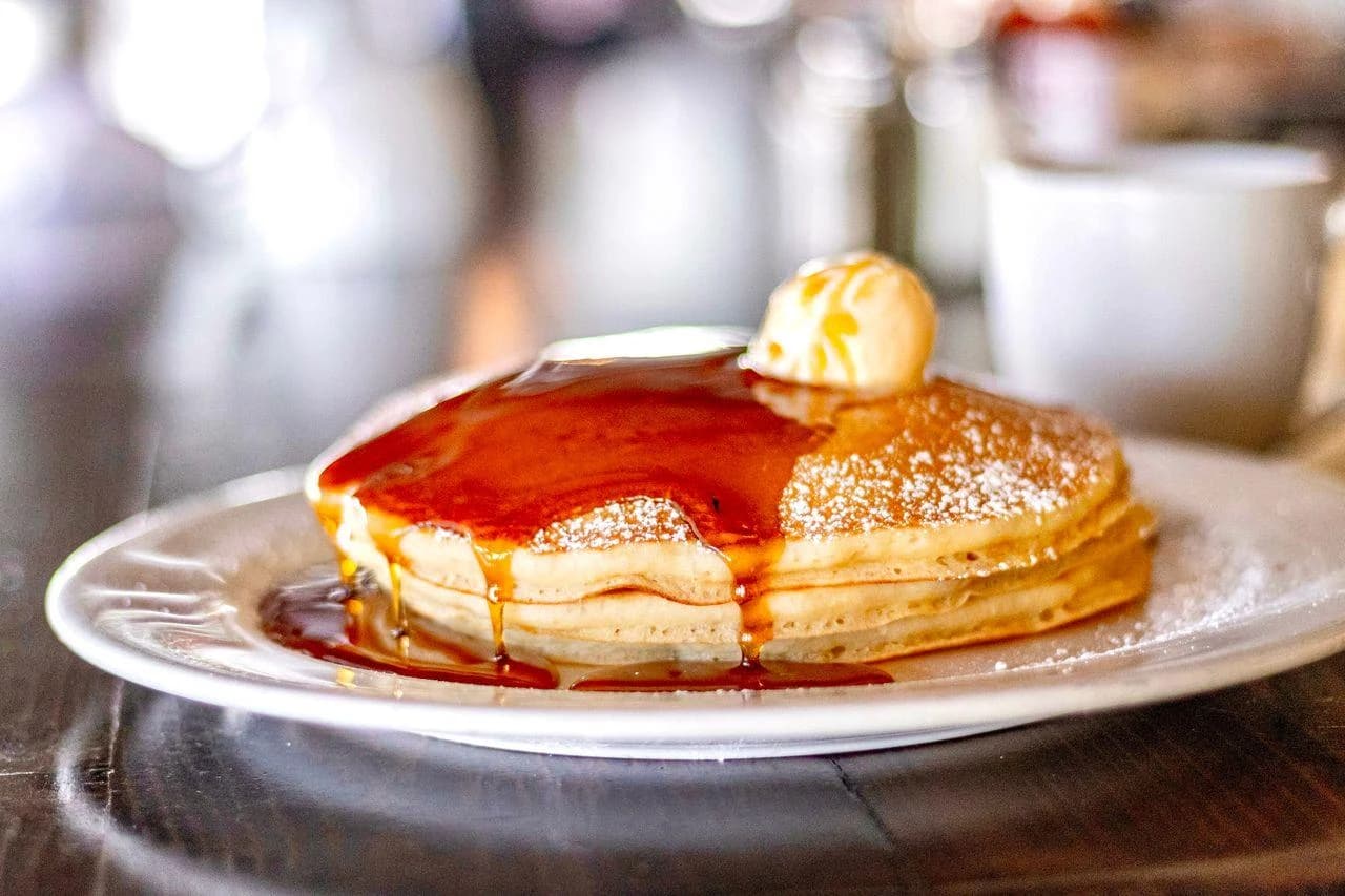 Stack of Killer Cafe breakfast pancakes dusted with powdered sugar, topped with butter and maple syrup, served for breakfast in Marina del Rey